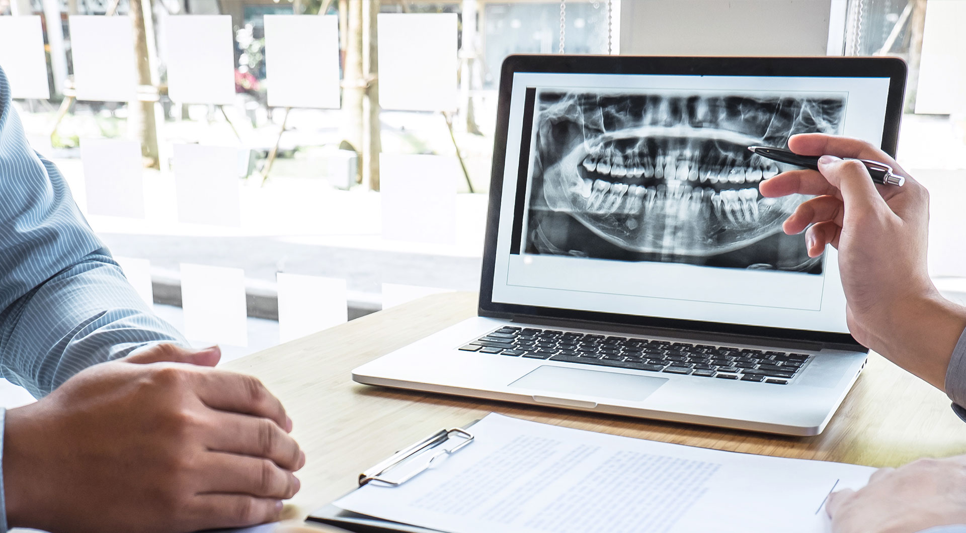 A split-screen image showing two different scenes on the left, a person working at a laptop with a presentation screen displaying an X-ray of a human jaw on the right, a close-up view of someone s hands pointing to the same X-ray displayed on the laptop.