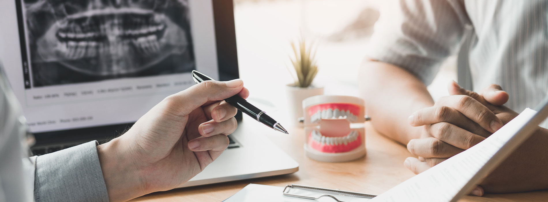 A blurred photo of two people sitting at a desk with a laptop, papers, and a cup of coffee, suggesting a professional work environment.